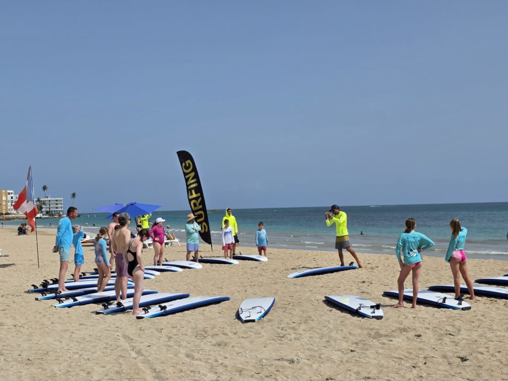 Surf students and WOW instructors standing with soft-top surfboards on Isla Verde beach