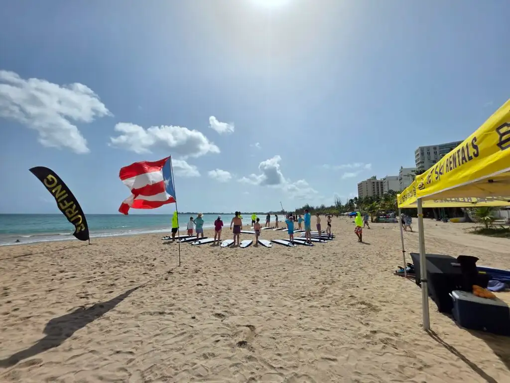 WOW surf lesson on the beach with surfboards lined up under the yellow tent and Puerto Rican flag